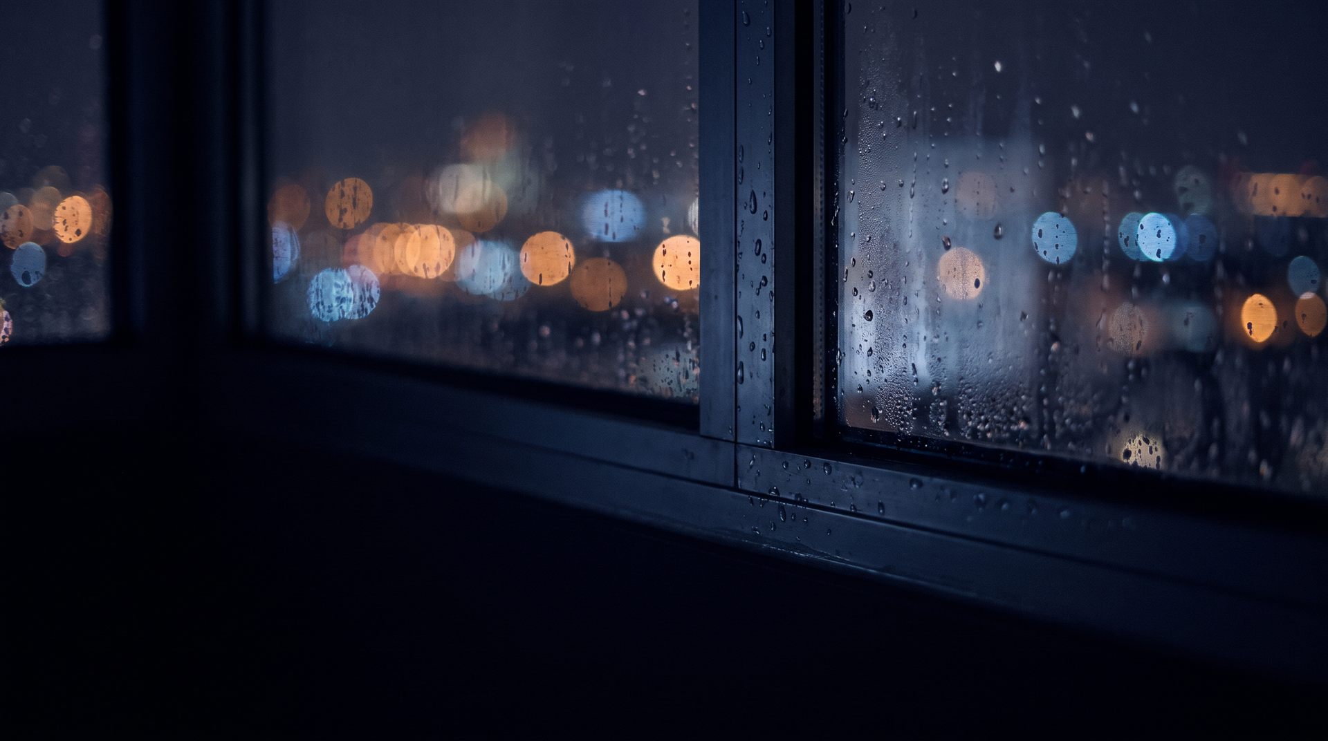 Rain running down the window of a dark high-rise office, city lights blurred beyond